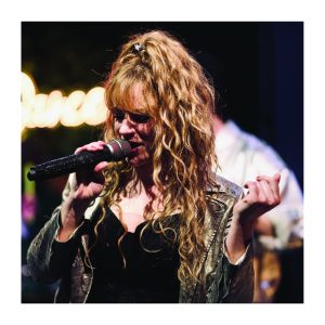 Sängerin von Music Nau Now mit Mikrofon bei einer energiegeladenen Live-Performance auf der Bühne.