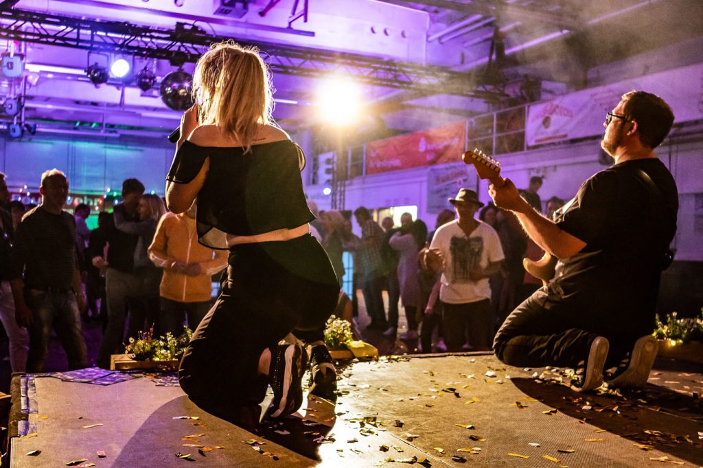 Sängerin und Gitarrist von Music Nau Now performen als Liveband auf der Bühne vor tanzendem Publikum.