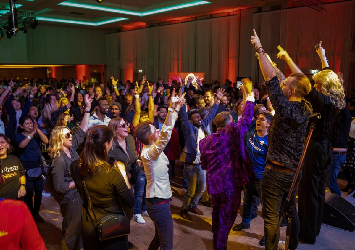 Großes tanzendes Publikum mit erhobenen Händen vor der Bühne bei einem energiegeladenen Live-Auftritt von Music Nau Now auf einem Corporate Event.